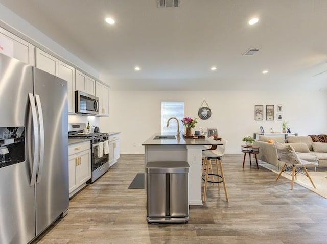 kitchen with a breakfast bar, appliances with stainless steel finishes, a kitchen island with sink, white cabinetry, and light wood-type flooring