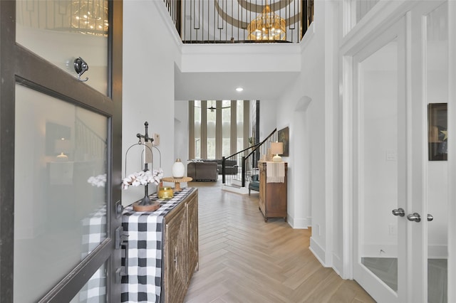 foyer entrance with a notable chandelier, a towering ceiling, and light parquet floors