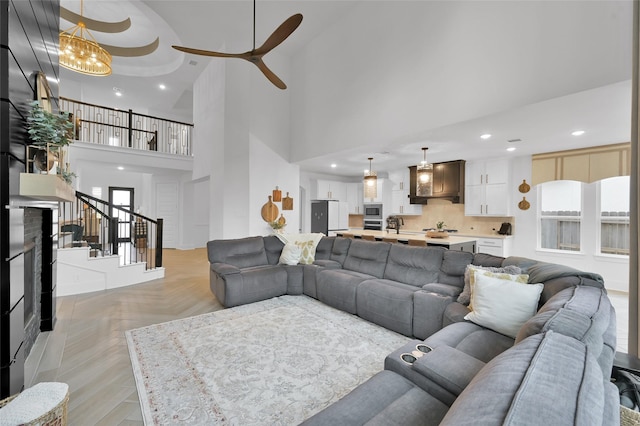 living room featuring ceiling fan with notable chandelier, a high ceiling, light parquet flooring, and a stone fireplace