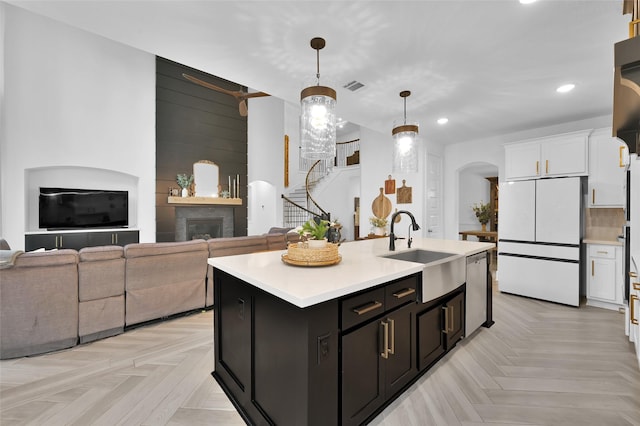 kitchen with white cabinets, white fridge, hanging light fixtures, and a center island with sink