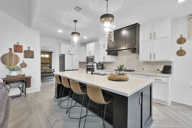 kitchen featuring stainless steel appliances, sink, a center island with sink, a chandelier, and white cabinetry