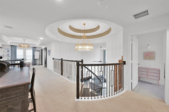 corridor with a chandelier, light carpet, and a tray ceiling