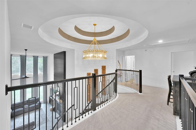 hall featuring a raised ceiling, light colored carpet, and an inviting chandelier