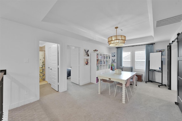 dining room with a barn door, a raised ceiling, and light colored carpet