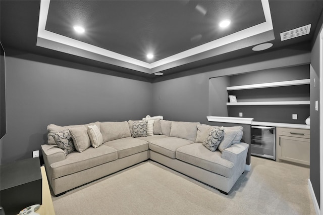 living room with bar, a raised ceiling, light carpet, and beverage cooler