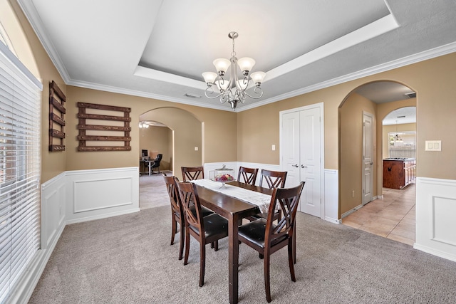 carpeted dining room with a tray ceiling, crown molding, and a notable chandelier