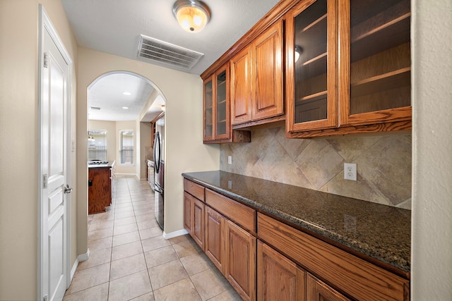 kitchen with light tile patterned floors, backsplash, and dark stone countertops