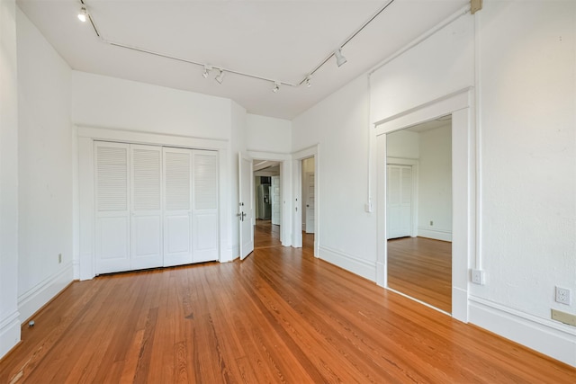 unfurnished bedroom with a closet, rail lighting, and hardwood / wood-style flooring