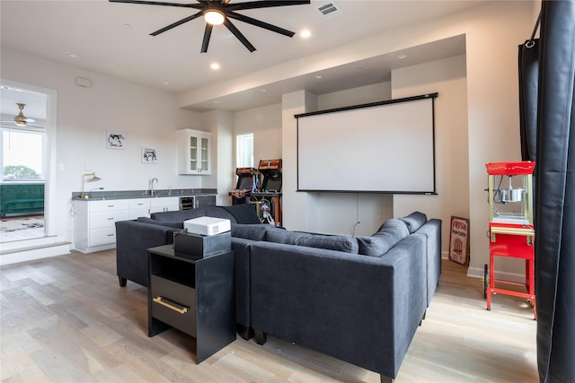 cinema room with light hardwood / wood-style floors, ceiling fan, and sink