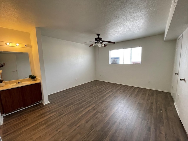 unfurnished bedroom featuring ceiling fan, sink, dark wood-type flooring, ensuite bathroom, and a textured ceiling