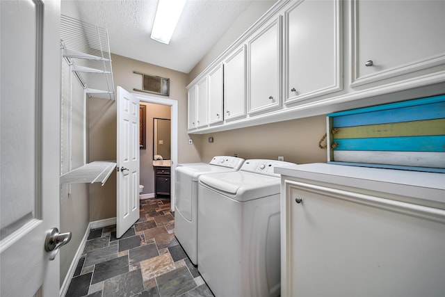 clothes washing area with cabinets, a textured ceiling, and washing machine and clothes dryer