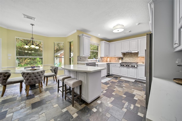 kitchen featuring pendant lighting, white cabinets, ornamental molding, tasteful backsplash, and a chandelier