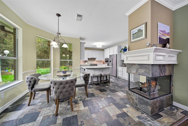 dining space with a multi sided fireplace, ornamental molding, and an inviting chandelier