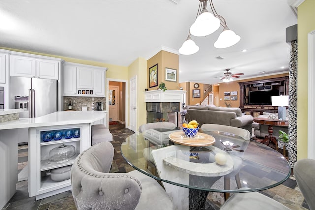 dining area featuring ceiling fan, a stone fireplace, and crown molding