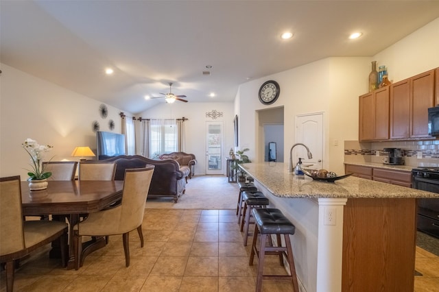 kitchen featuring sink, stove, backsplash, an island with sink, and vaulted ceiling