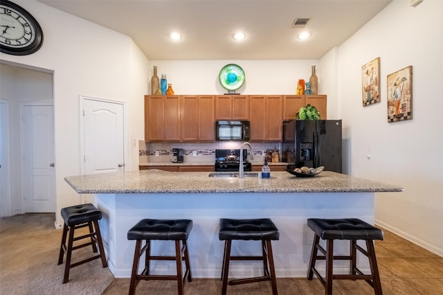 kitchen featuring a breakfast bar, sink, a center island with sink, decorative backsplash, and black appliances