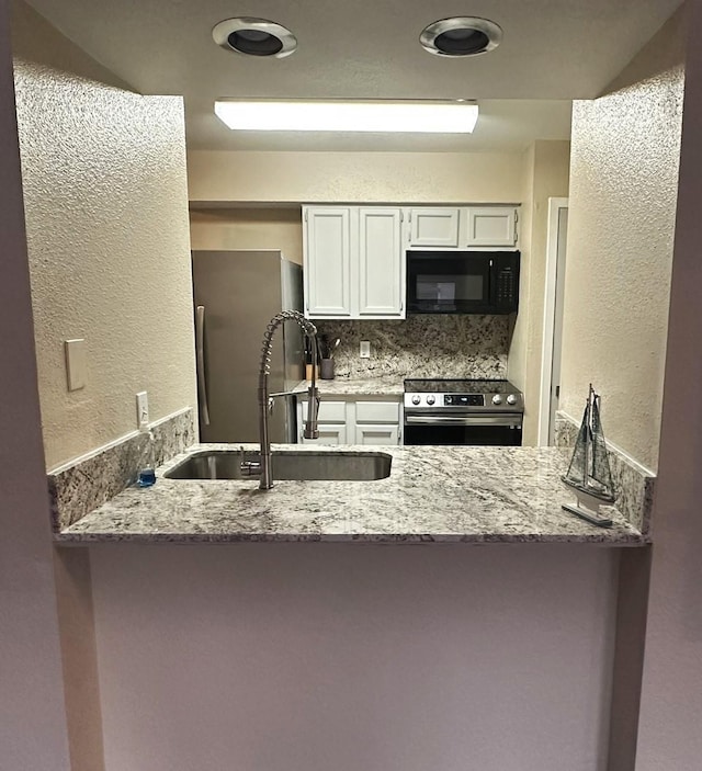 kitchen featuring light stone countertops, white cabinetry, sink, stainless steel appliances, and decorative backsplash