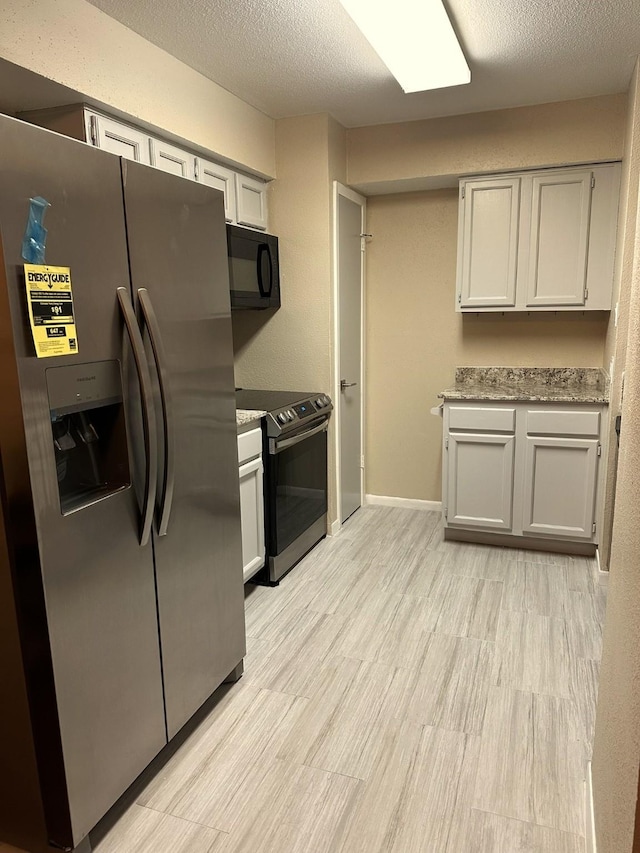 kitchen with light stone countertops, appliances with stainless steel finishes, light wood-type flooring, and a textured ceiling