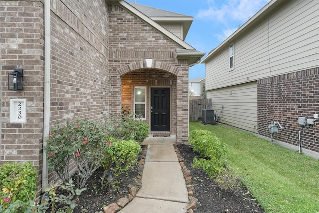 view of exterior entry featuring a lawn and central AC unit