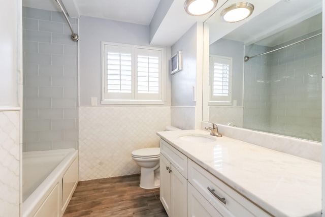 full bathroom with vanity, tiled shower / bath combo, toilet, tile walls, and wood-type flooring