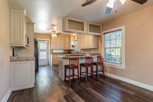 kitchen featuring kitchen peninsula, light stone countertops, dark wood-type flooring, fridge, and a breakfast bar area