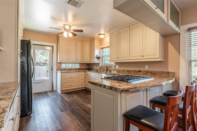 kitchen featuring ceiling fan, a kitchen breakfast bar, black fridge, light stone counters, and dark hardwood / wood-style flooring