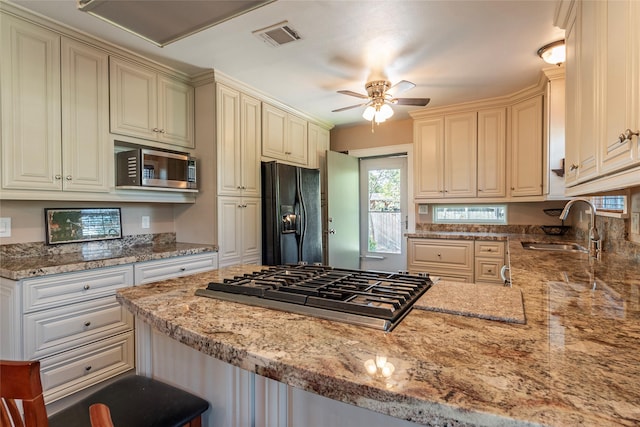 kitchen with kitchen peninsula, appliances with stainless steel finishes, ceiling fan, sink, and a breakfast bar area