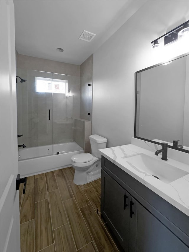 full bathroom with enclosed tub / shower combo, toilet, vanity, visible vents, and wood tiled floor