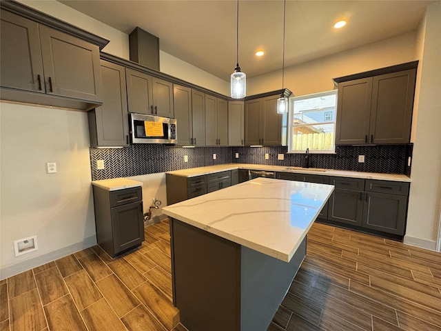 kitchen with a center island, dark wood-type flooring, sink, hanging light fixtures, and light stone counters