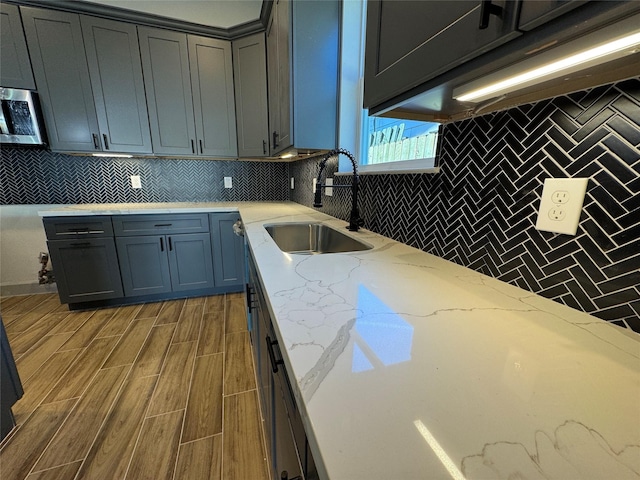 kitchen with sink, light stone counters, dark hardwood / wood-style flooring, gray cabinets, and decorative backsplash