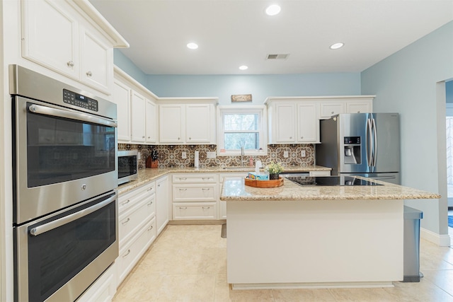 kitchen featuring sink, appliances with stainless steel finishes, a kitchen island, light stone counters, and white cabinetry