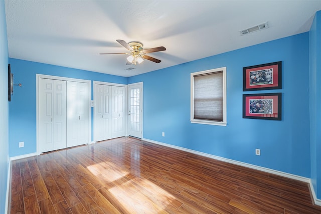 unfurnished bedroom featuring multiple closets, ceiling fan, and hardwood / wood-style flooring