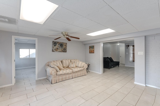 living room with a drop ceiling, ceiling fan, and brick wall