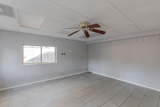 unfurnished room featuring a paneled ceiling, ceiling fan, and brick wall