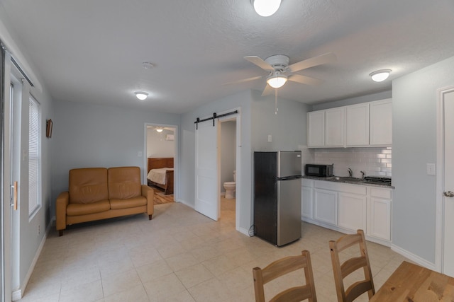 kitchen featuring stainless steel refrigerator, white cabinetry, ceiling fan, a barn door, and decorative backsplash