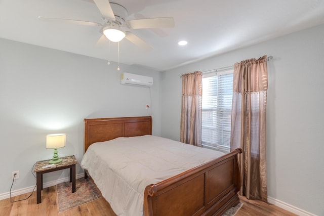 bedroom with ceiling fan, a wall unit AC, and light hardwood / wood-style flooring