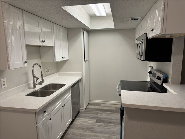 kitchen featuring sink, light hardwood / wood-style flooring, a textured ceiling, appliances with stainless steel finishes, and white cabinetry