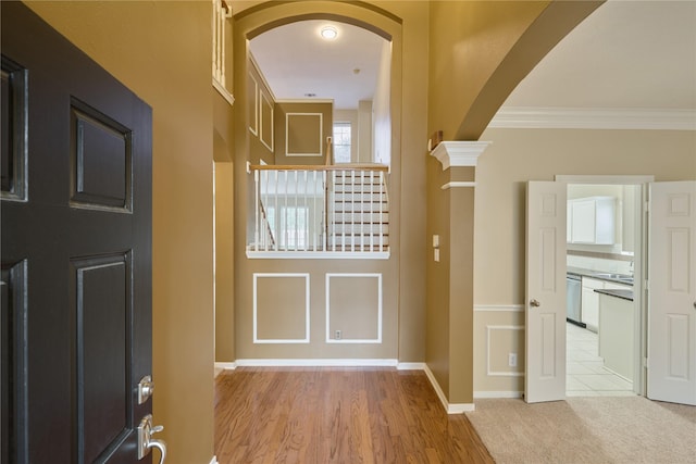 foyer entrance featuring decorative columns, ornamental molding, and light hardwood / wood-style flooring