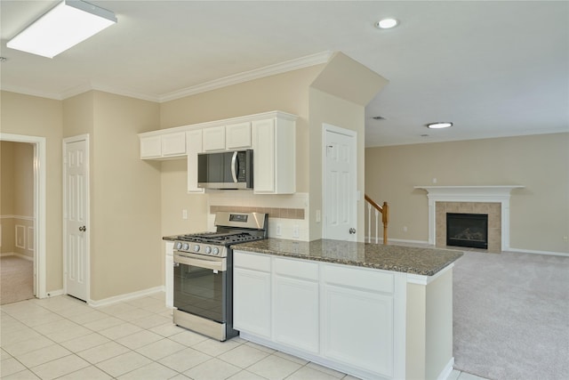 kitchen featuring white cabinets, ornamental molding, a fireplace, appliances with stainless steel finishes, and light colored carpet