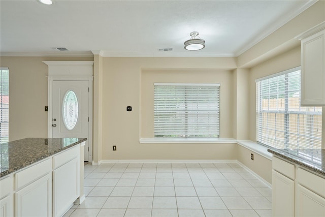 kitchen featuring white cabinetry, a wealth of natural light, dark stone counters, and crown molding