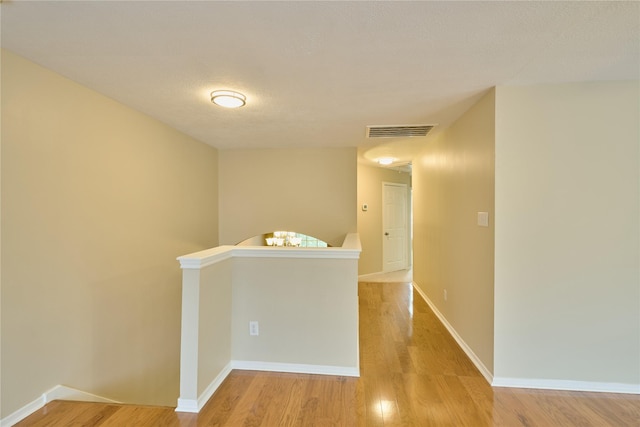 hallway with a textured ceiling and light hardwood / wood-style flooring