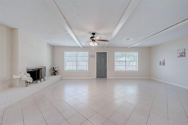 unfurnished living room featuring ceiling fan, a brick fireplace, plenty of natural light, a textured ceiling, and light tile patterned floors