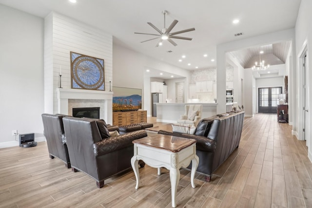 living room with french doors, light hardwood / wood-style flooring, vaulted ceiling, and ceiling fan with notable chandelier