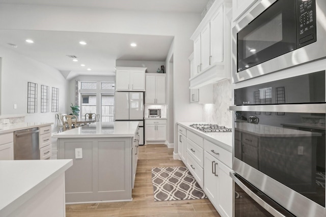 kitchen with decorative backsplash, appliances with stainless steel finishes, white cabinets, light hardwood / wood-style floors, and a kitchen island