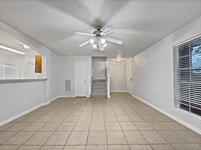 unfurnished living room with ceiling fan, light tile patterned floors, and a textured ceiling