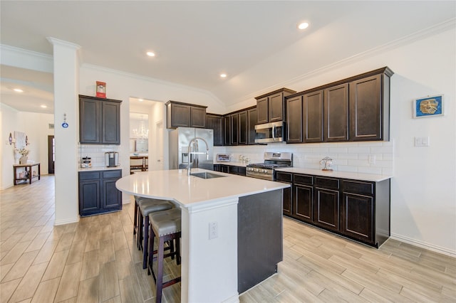 kitchen featuring a breakfast bar, a center island with sink, sink, decorative backsplash, and appliances with stainless steel finishes