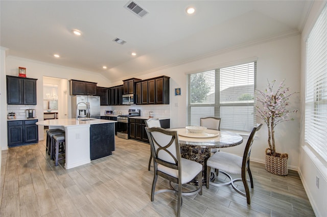 kitchen with backsplash, stainless steel appliances, light hardwood / wood-style flooring, lofted ceiling, and an island with sink