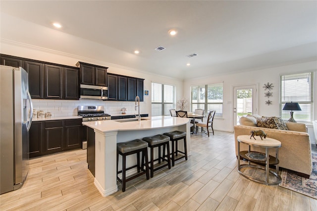 kitchen with light hardwood / wood-style floors, an island with sink, appliances with stainless steel finishes, and a breakfast bar area