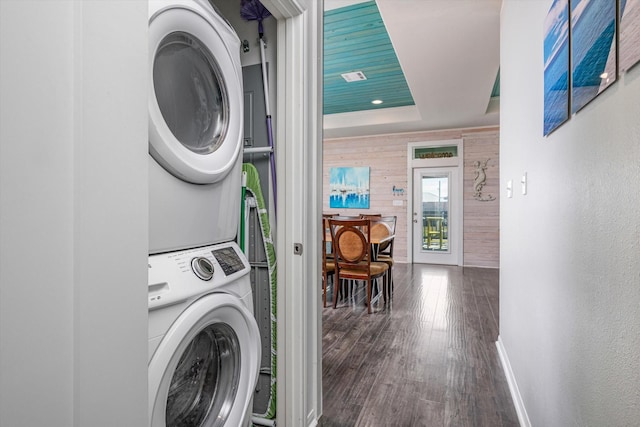 laundry area with wood walls, dark wood-type flooring, and stacked washer / drying machine