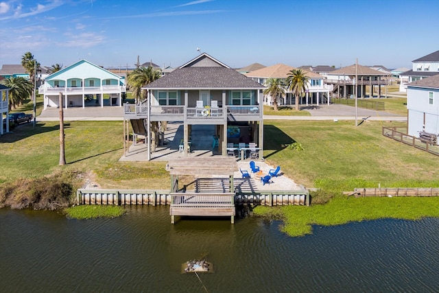 rear view of property with a deck with water view, a patio area, and a lawn